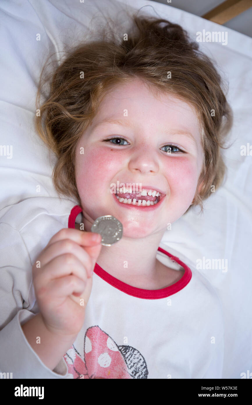 Giovane ragazza sorridente per rivelare la mancanza di un dente anteriore / denti dente, mentre tenendo un 50p / cinquanta pence moneta in cui è arrivato dal dente di fata sotto il suo cuscino. Regno Unito (111) Foto Stock