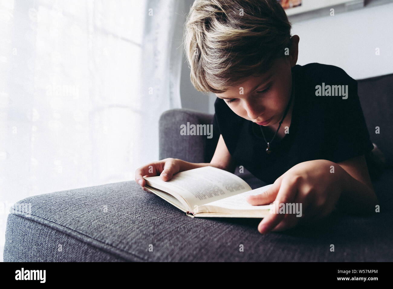 Vista ravvicinata del biondo ragazzo lettura libro studente concentrato sdraiato legge la lezione comodamente rilassati, assiduo bambino legge una storia, giovane Foto Stock