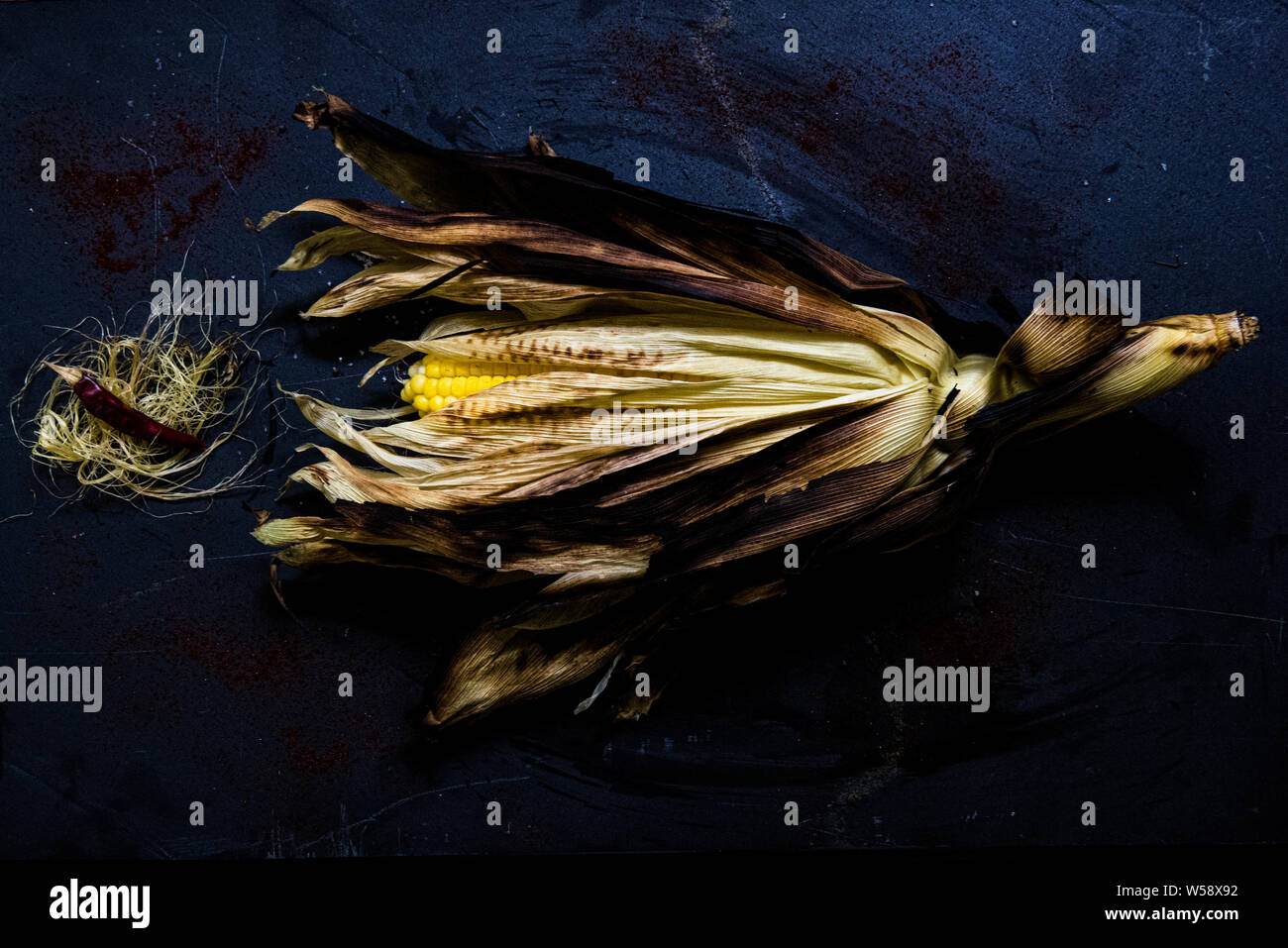 Carbonizzati orecchio di mais con sansa e pepe di piccole dimensioni su sfondo blu Foto Stock