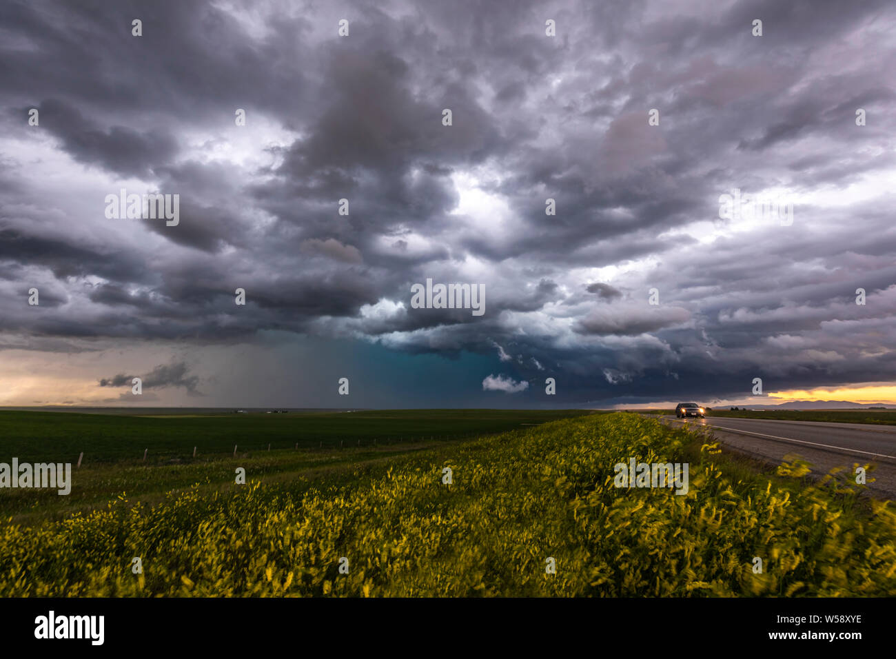 Pesante cielo cloud su strada e campo giallo con auto di avvicinamento Foto Stock