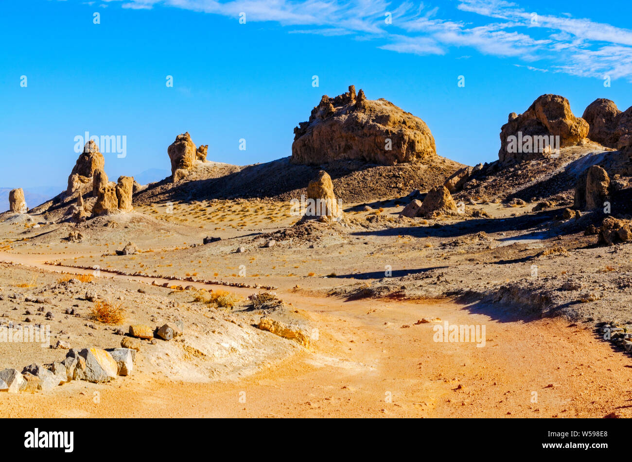 Marrone rossiccio strada sterrata che conduce verso il deserto formazioni rocciose nella luce del sole di mattina sotto cieli azzurri. Foto Stock