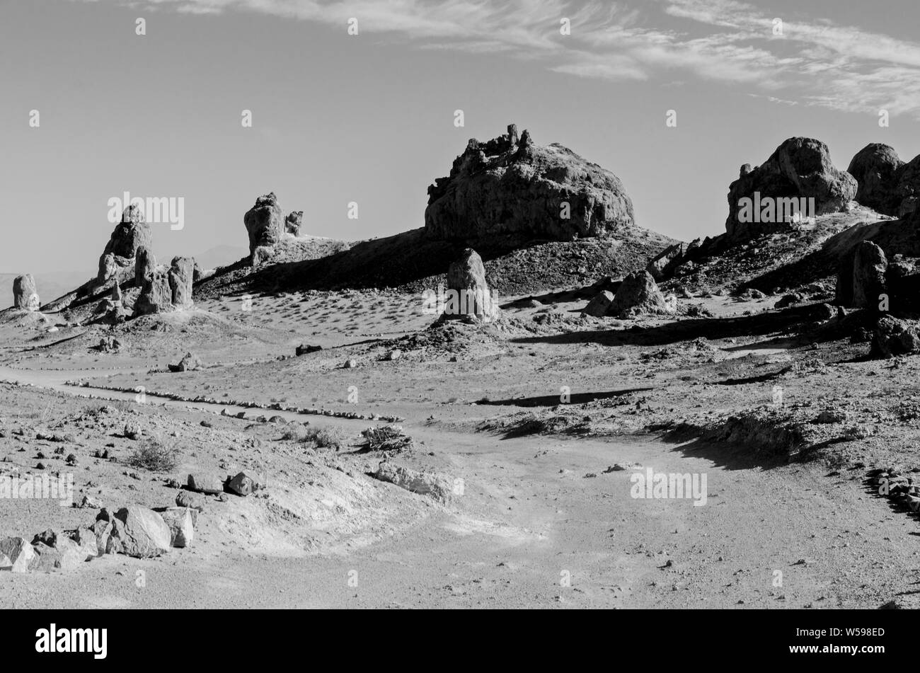 Le formazioni rocciose che gettano ombre, strada sterrata che conduce attraverso l'arido deserto desolato terreno. In bianco e nero. Foto Stock