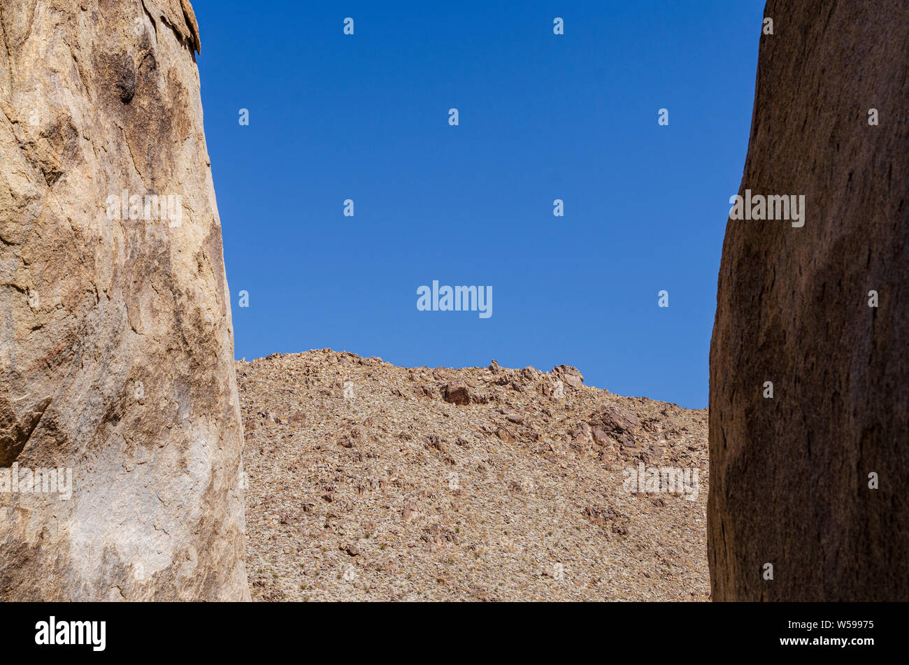Guardando attraverso due grandi massi a arido deserto al di là della montagna sotto i cieli blu. Foto Stock