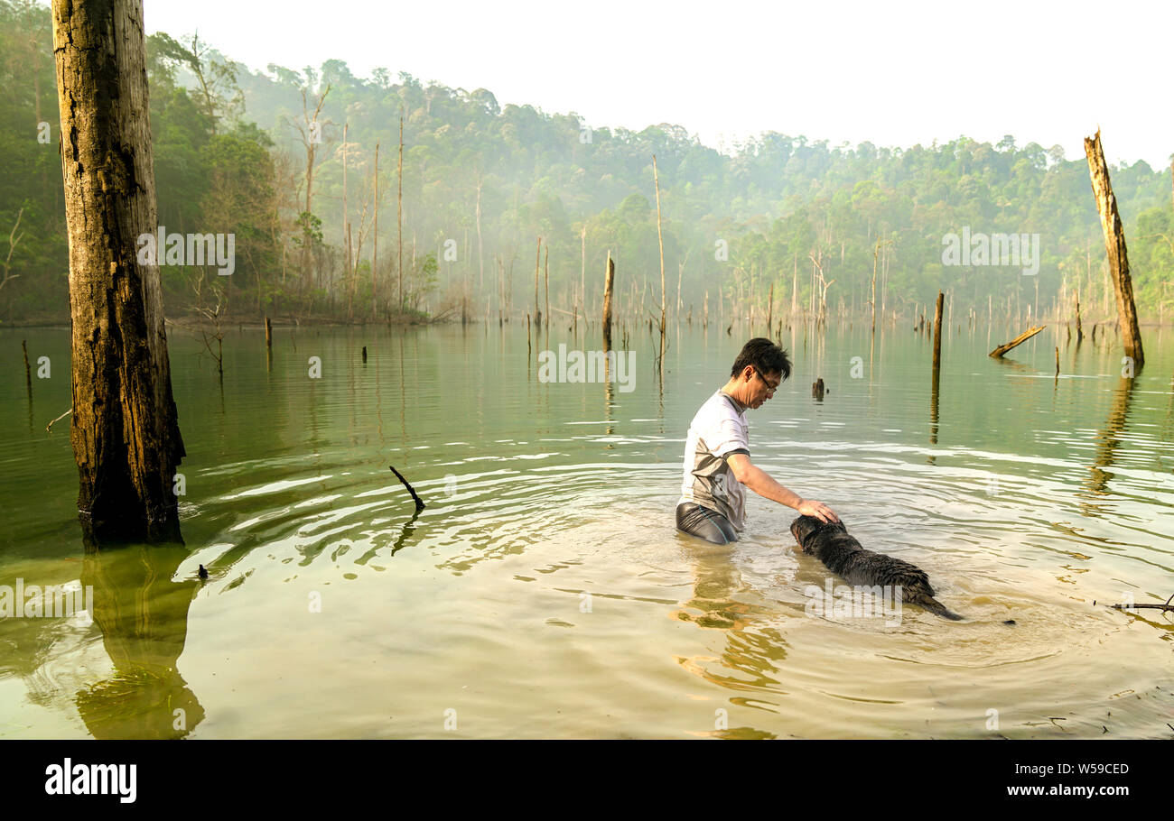 Uomo di giocare e nuotare con il cane in un lago. Ricreazione e svago del concetto. Foto Stock