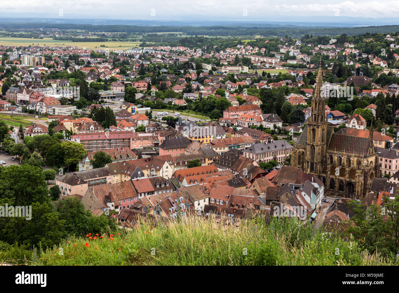 Affacciato sulla pittoresca città alsaziana di Thann, Francia tra cui la medievale San Teobaldo Chiesa su un nuvoloso giorno francese. Foto Stock