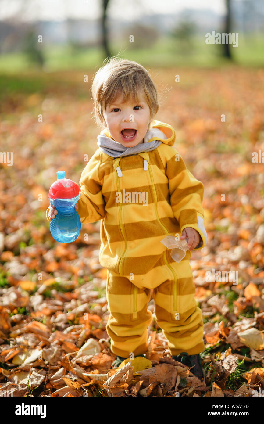 Concetto: famiglia, bambini. Felice piccolo bambino, baby boy con acqua in bottiglia ridendo e giocando in autunno la natura a piedi all'aperto presso il park Foto Stock