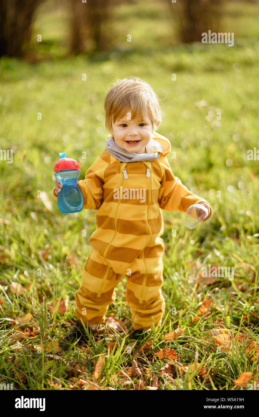 Concetto: famiglia, bambini. Felice piccolo bambino, baby boy con acqua in bottiglia ridendo e giocando in autunno la natura a piedi all'aperto presso il park Foto Stock