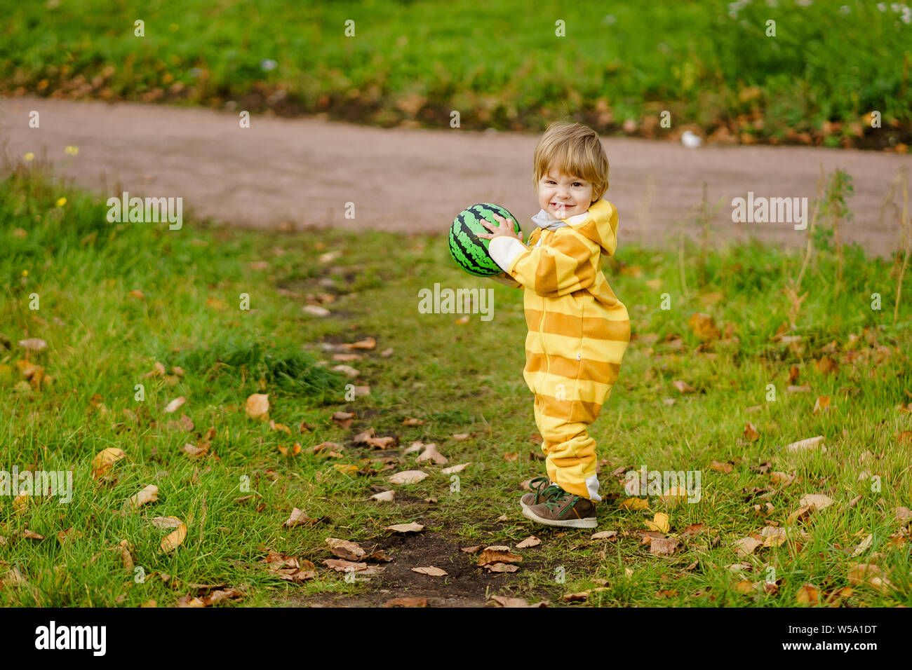 Concetto: famiglia, bambini. Felice piccolo bambino, baby boy ridendo e giocando con la palla verde in autunno la natura a piedi all'aperto presso il park Foto Stock