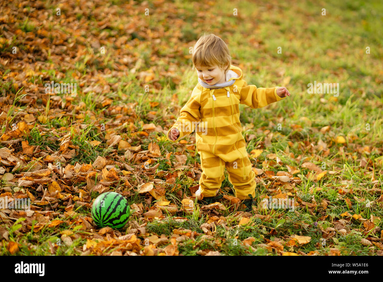 Concetto: famiglia, bambini. Felice piccolo bambino, baby boy ridendo e giocando con la palla verde in autunno la natura a piedi all'aperto presso il park Foto Stock