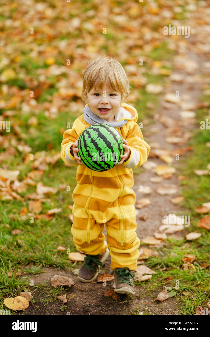 Concetto: famiglia, bambini. Felice piccolo bambino, baby boy ridendo e giocando con la palla verde in autunno la natura a piedi all'aperto presso il park Foto Stock