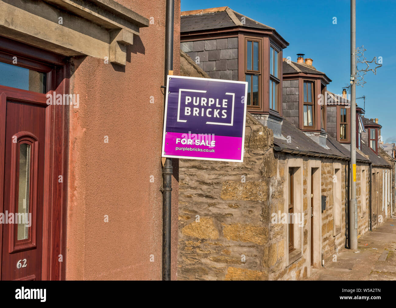 Mattoni di colore viola in vendita segno di una strada con case e il segno sul muro di una casa Foto Stock