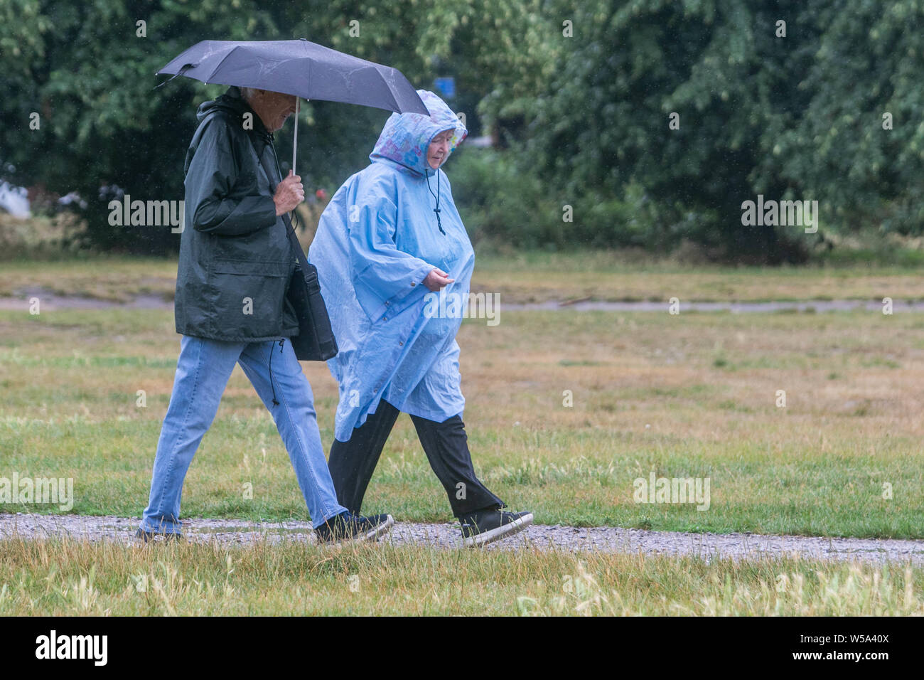 Wimbledon Londra UK. Il 27 luglio 2019. Un uomo con una donna umbrellaa e indossando un poncho a piedi su Wimbledon Common in una piovosa mattinata come temperature beging raffreddare a seguito di una ondata di caldo record impostato su giovedì .Credito: amer ghazzal/Alamy Live News Foto Stock