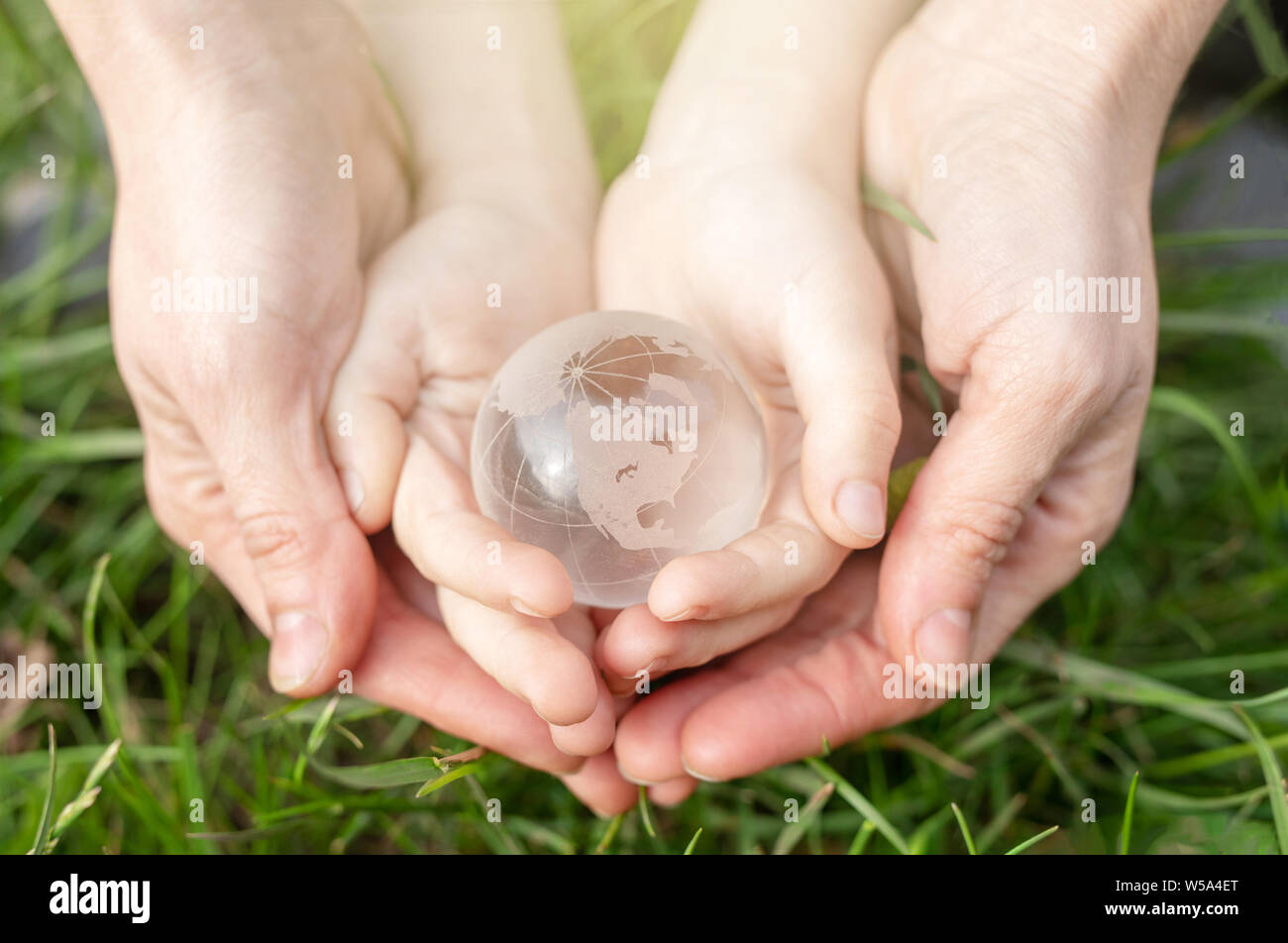 Salvare la terra consept. Il concetto di ambiente. Globo di vetro nelle mani di un bambino e donne sullo sfondo di erba verde Foto Stock