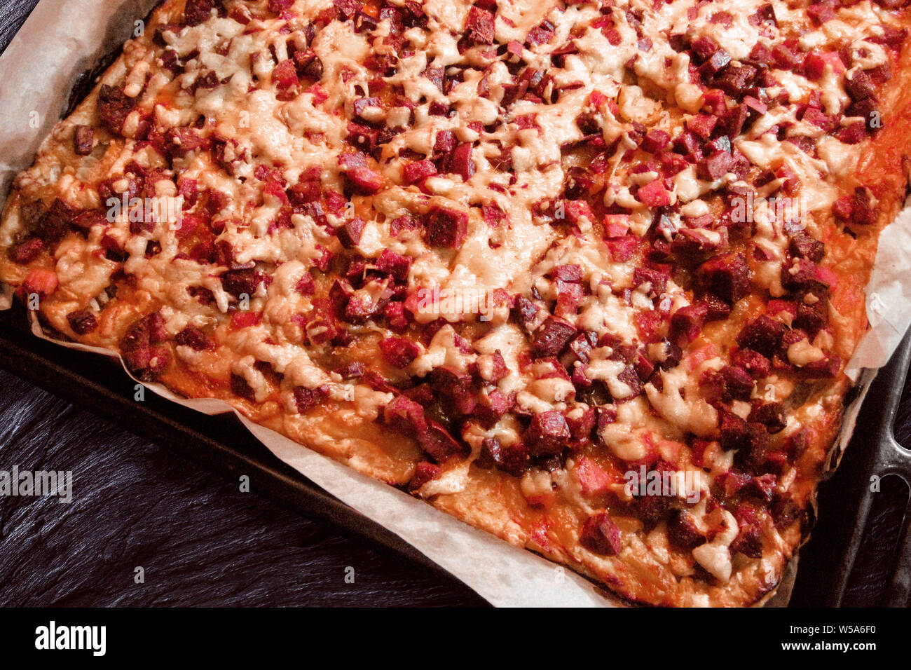Pizza cotta al forno con carne e salumi e formaggi. Home cucina a vista su  ferro pentola di cottura il vassoio e la cucina la carta pergamena. Calorie  malsano cibo spazzatura. Ri