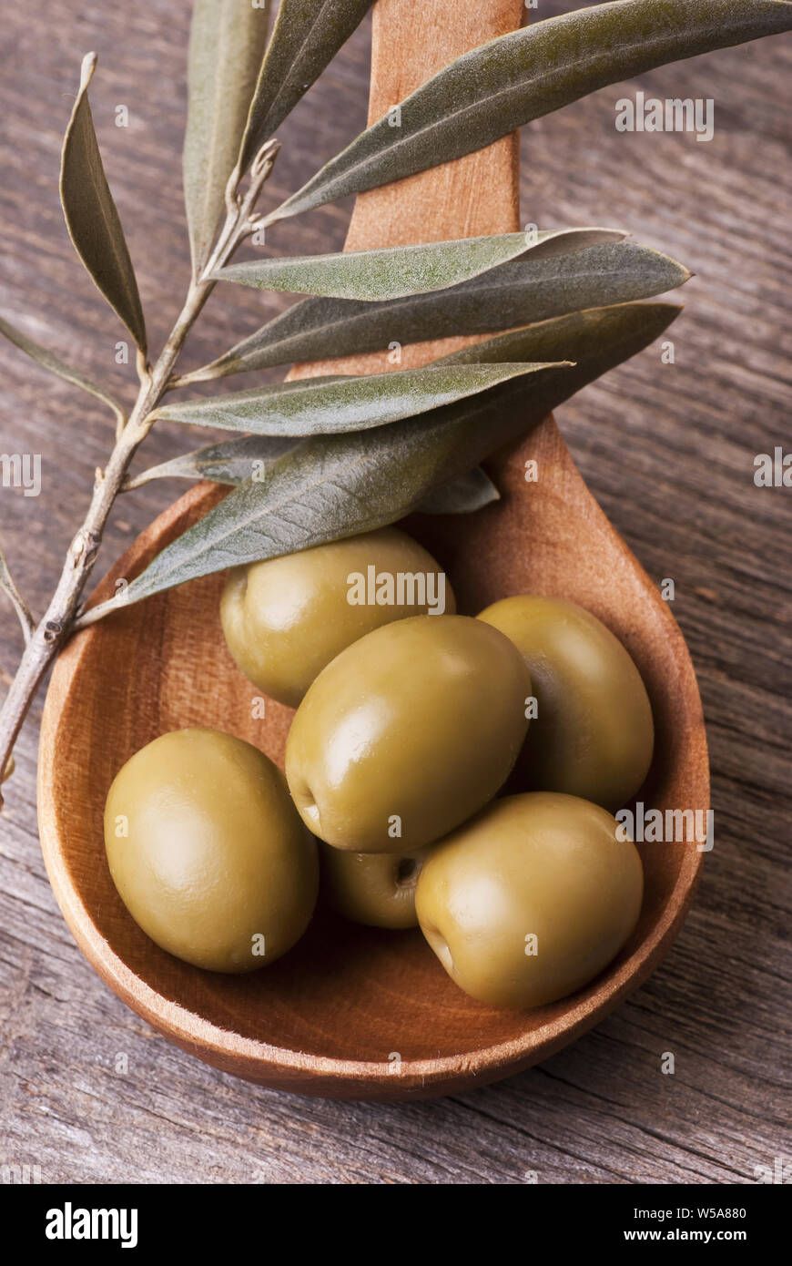 Olive verdi in il cucchiaio di legno con olio di oliva ramoscello su tavola in legno rustico Foto Stock