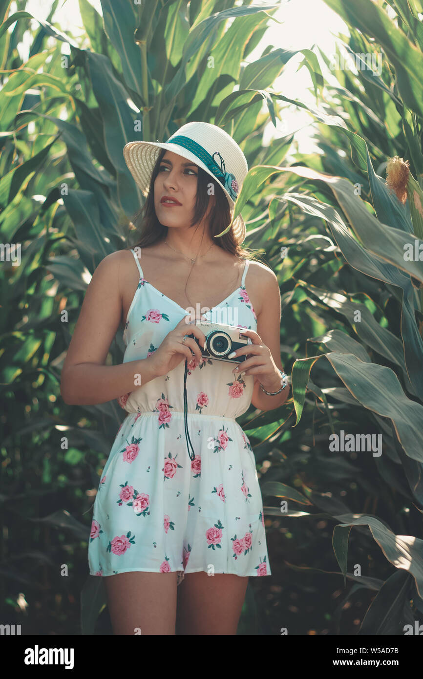 Outdoor Lifestyle ritratto di una giovane bella bruna ragazza con vintage fotocamera foto indossando un abito fiorito e cappello per il sole Foto Stock