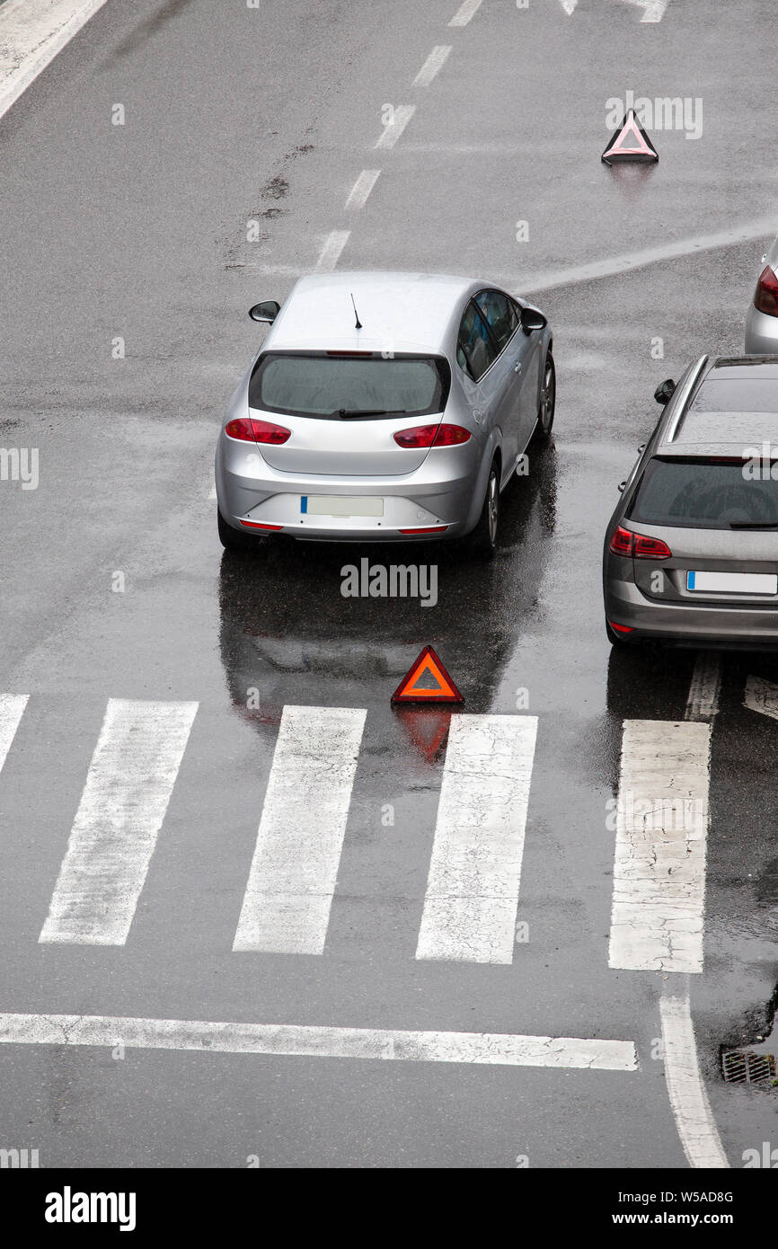 Scena di un ripartiti in auto su una strada di città strada vicino a un crosswalk e con un triangolo rosso per avvertire gli altri utenti della strada. Giorno di pioggia. Spazio di copia Foto Stock