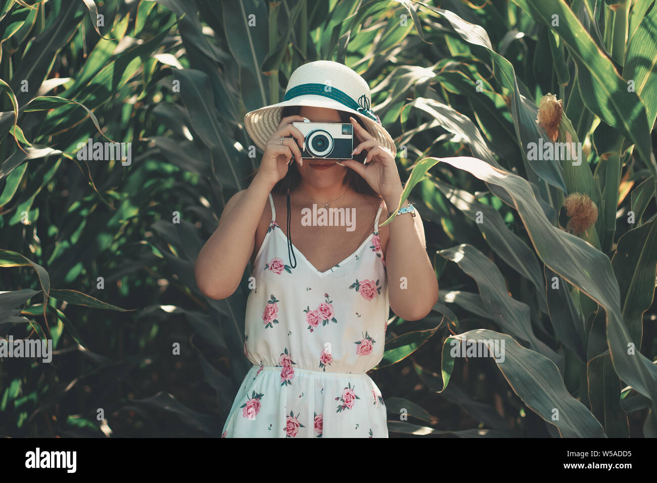 Uno stile di vita all'aperto il ritratto di una giovane donna con un vintage fotocamera foto indossando bianco abito fiorito e cappello per il sole Foto Stock