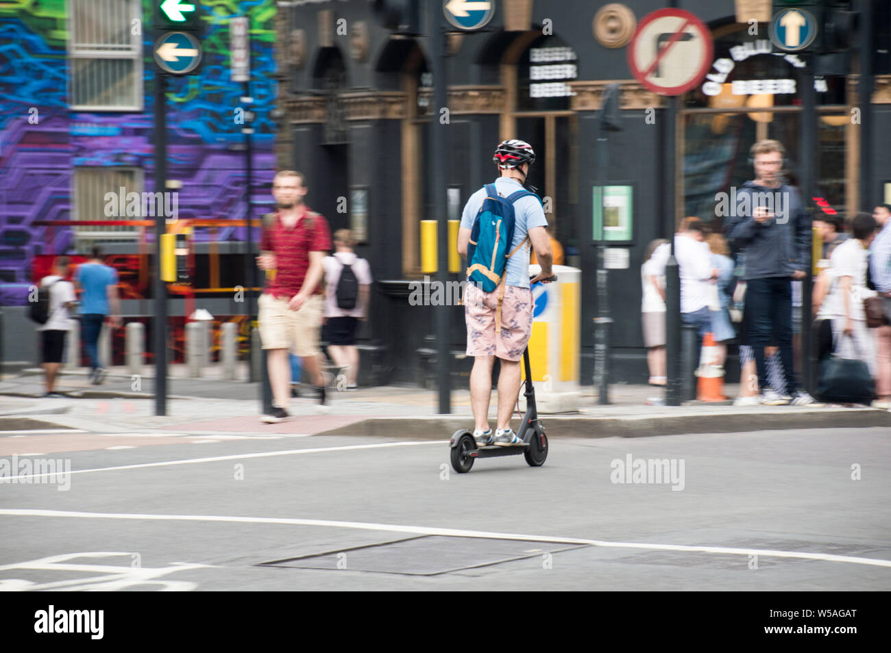 Giro in scooter elettrico o in scooter da un maschio adulto Con casco e borsa in London City Road Foto Stock