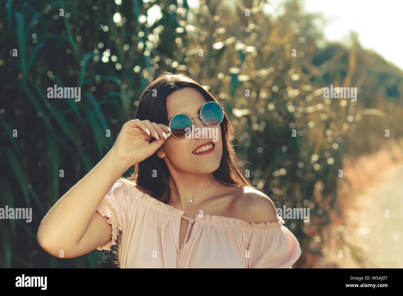 Ritratto di una giovane donna sorridente e indossando occhiali da sole all'aperto in un brillare di giorno Foto Stock