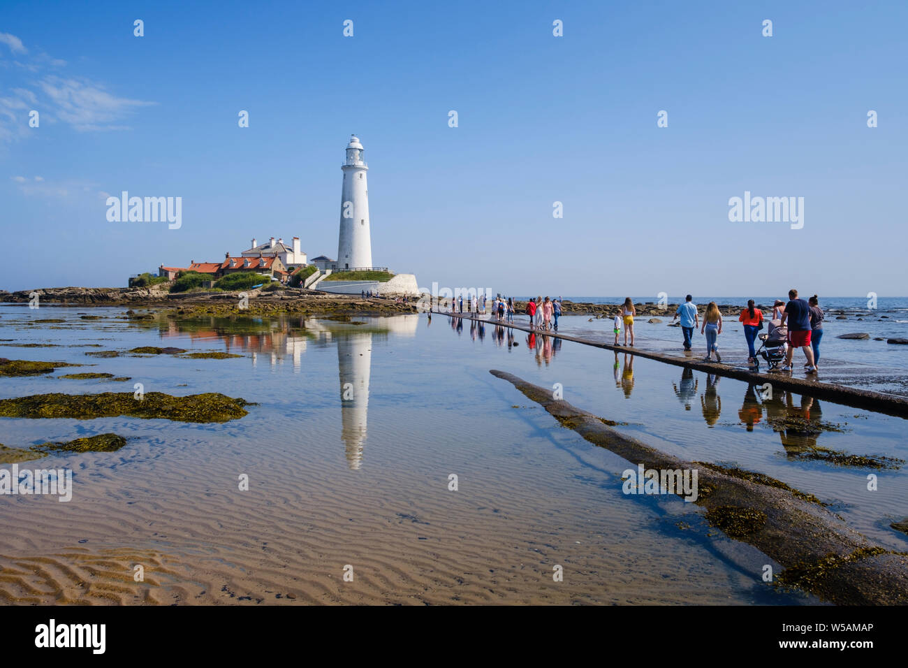 Il Northumberland coast - trippers giorno i turisti e le famiglie a piedi attraversata la strada rialzata a St Mary's Faro a Whitley Bay North Tyneside Foto Stock