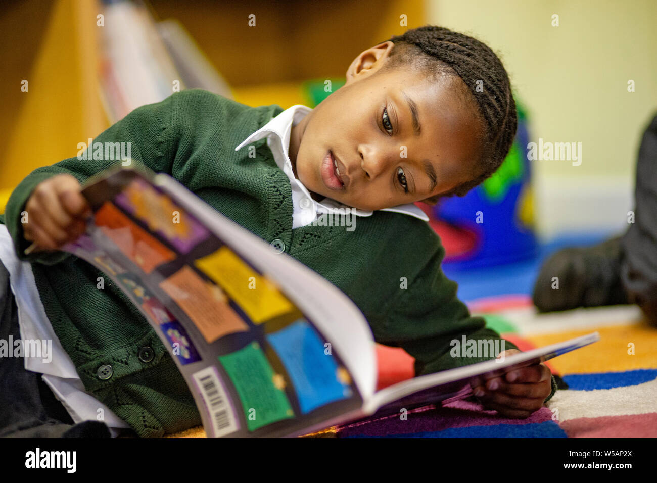Una ragazza afro-caraibica della lettura in una scuola primaria BIBLIOTECA NEL REGNO UNITO Foto Stock