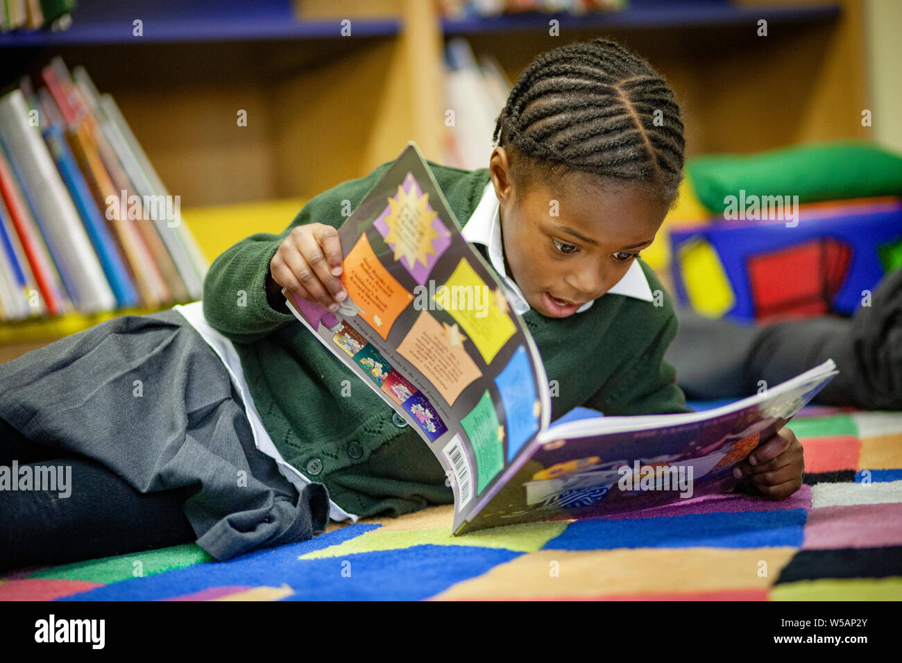 Una ragazza afro-caraibica della lettura in una scuola primaria BIBLIOTECA NEL REGNO UNITO Foto Stock