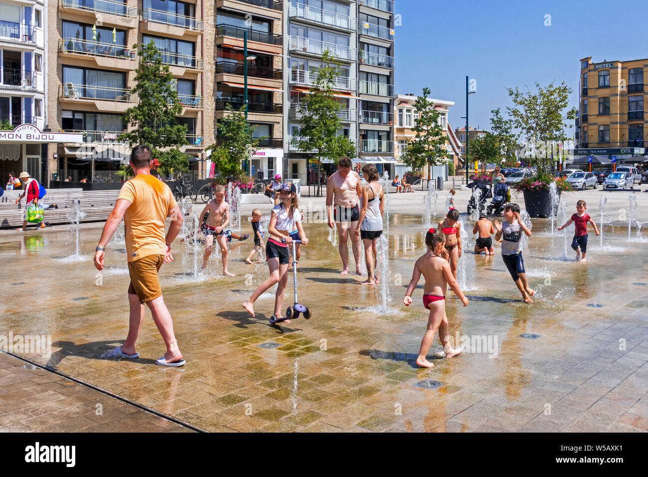 Adulti e bambini a giocare in acqua di fontana per rinfrescarsi nelle temperature di brucianti durante l'ondata di caldo in estate Foto Stock