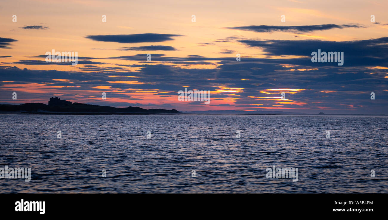 Tramonto dietro il castello di Bamburgh e Lindisfarne sulla costa di Northumberland Foto Stock