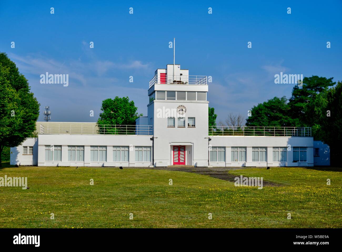 Weybridge, Surrey, Regno Unito - Luglio 23, 2019: Art deco ex airfield torre di controllo dipinto di bianco con orologio, erba davanti con alberi e briga Foto Stock