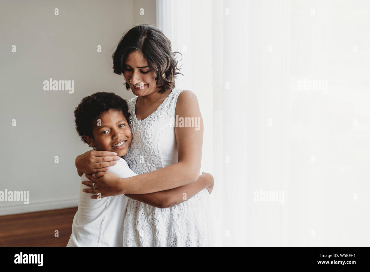 Madre abbracciando la scuola in età figlio nella sorridente abbraccio in studio Foto Stock
