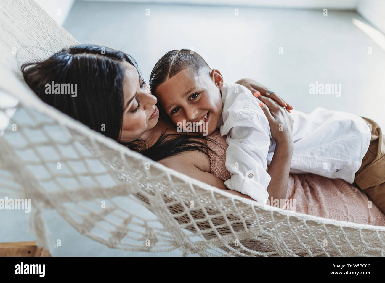 Madre e figlio giovane cuddling mentre posa in amaca in studio Foto Stock