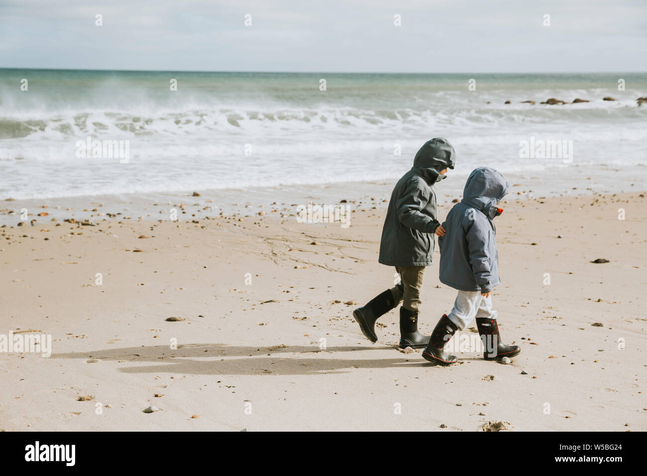 Due ragazzi a piedi lungo la spiaggia con le onde del mare Foto Stock