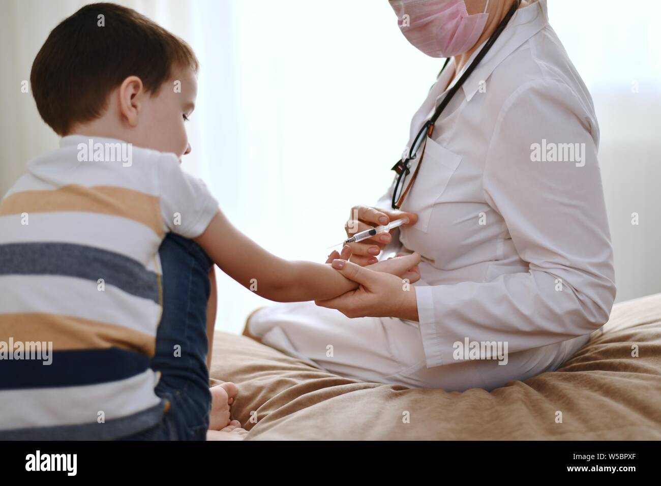 La vaccinazione di un bambino al di sotto dei cinque anni da parte di un medico in casa. Dimostrazione di vaccinazione con una siringa in mano del ragazzo. Foto Stock