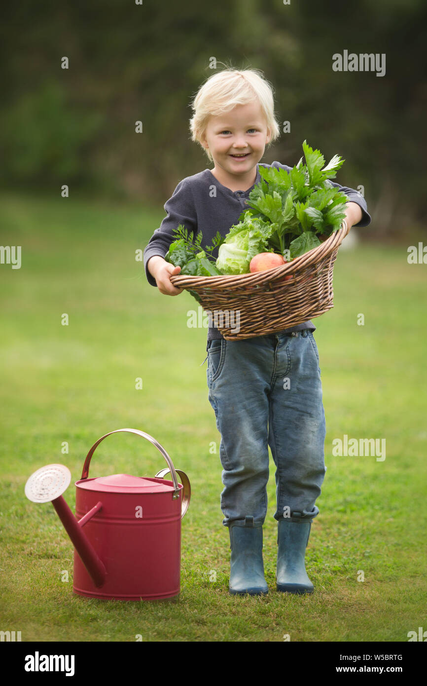 Felice ragazzo biondo mostra con orgoglio il suo raccolto di frutta e verdura Foto Stock