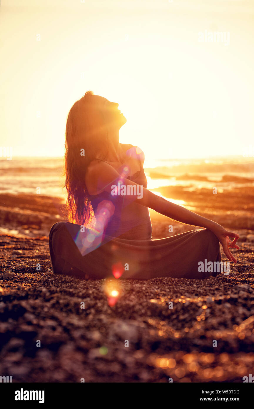 La meditazione yoga donna nella beatitudine di energia luminosa sulla spiaggia al tramonto. Foto Stock
