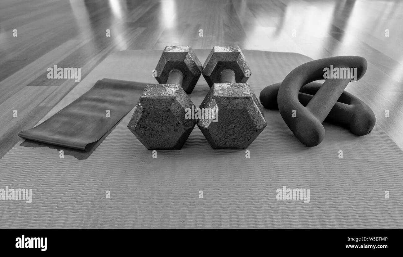 Versione in bianco e nero di chiudere una coppia di manubri, esercizio con elastici Theraband bande e un materassino yoga su pavimento in legno duro Foto Stock