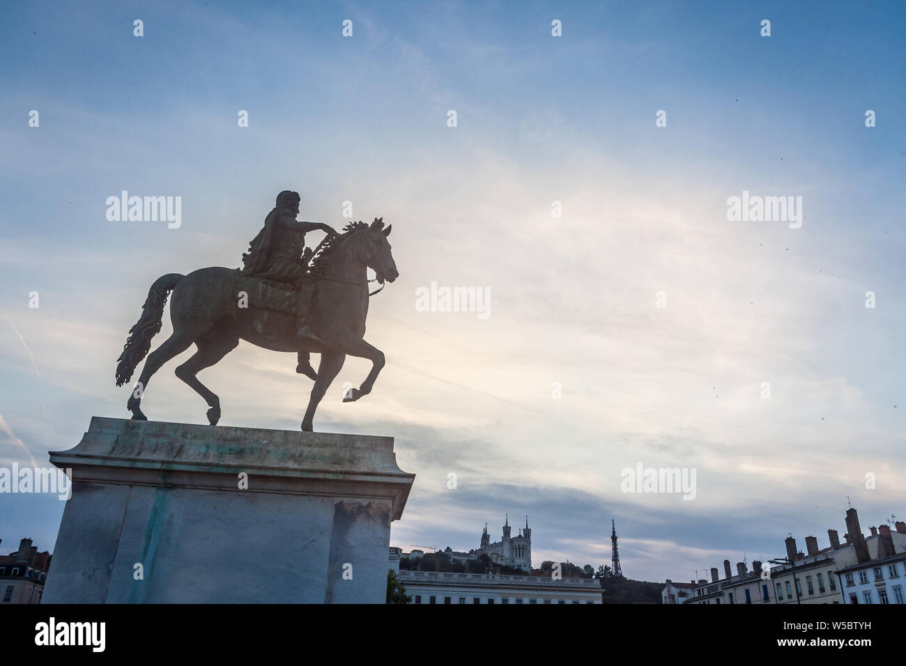 Il Roi Louis XIV statua sul display della Place Bellecour Square, nel centro di Lione, in Francia, con la Basilica di Notre Dame de Fourviere chiesa in backgrou Foto Stock