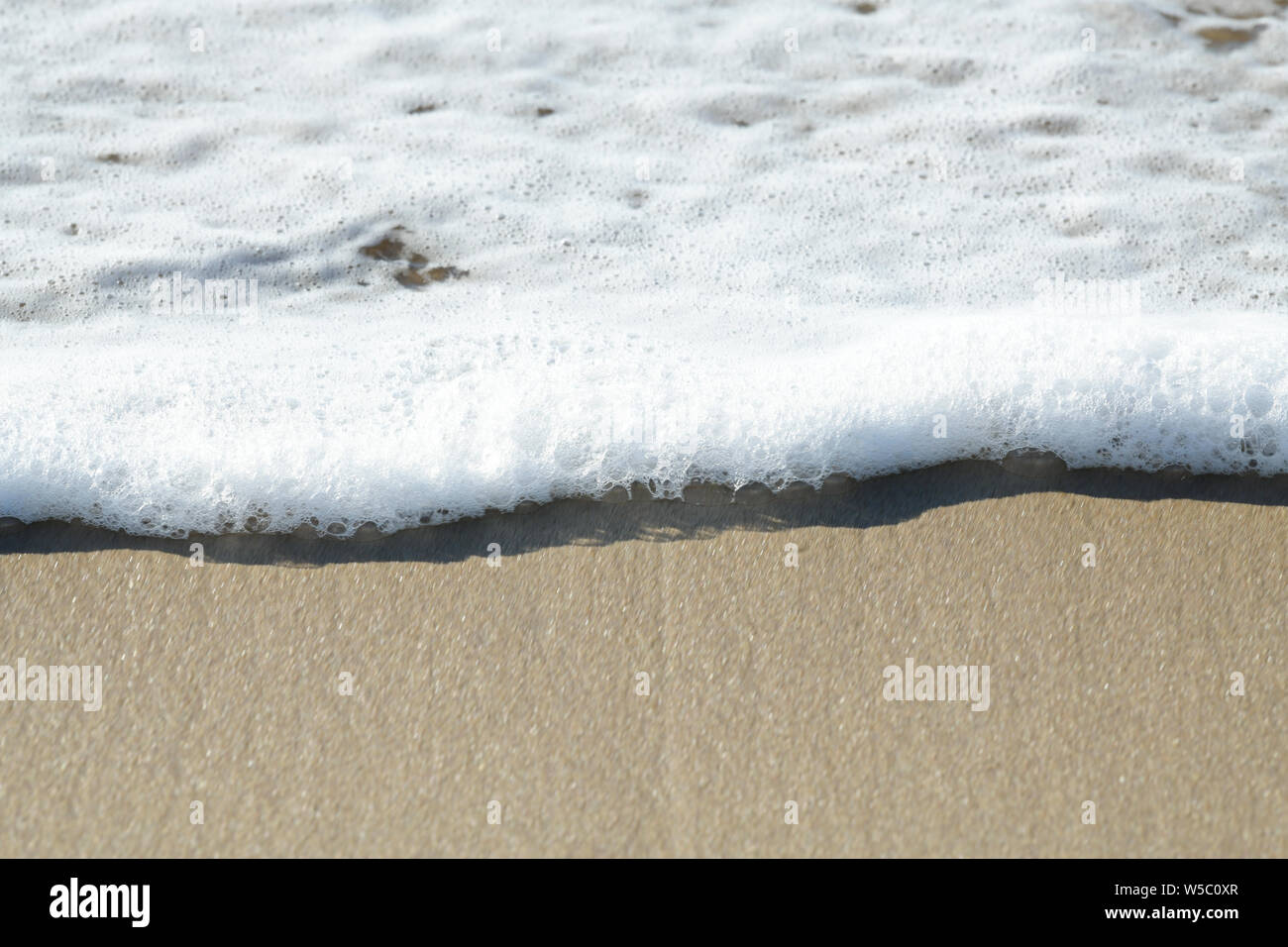 Close up, dettaglio, schiuma e bolle di onda trascorso il lavaggio sulla sabbia di mare, astratta, sfondi Foto Stock