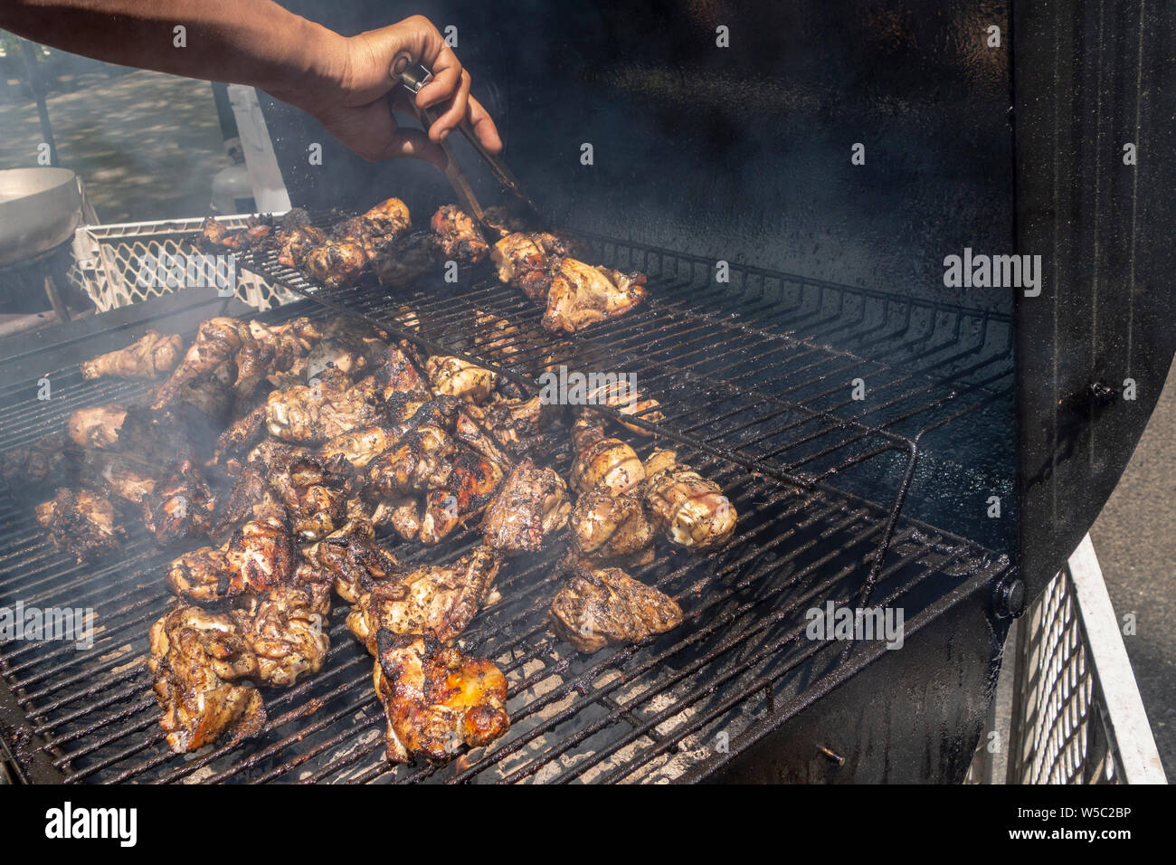 Il fumo di carbone per barbecue grill con un mans girando a mano il pollo di cottura Foto Stock