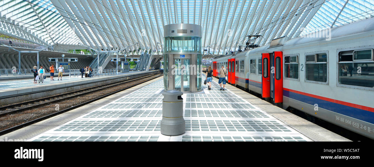 Vista posteriore di uomo e donna giovane a piedi lungo ampia piattaforma dopo viaggio ferroviario accanto al treno lungo al design moderno Liège Belgio station building UE Foto Stock