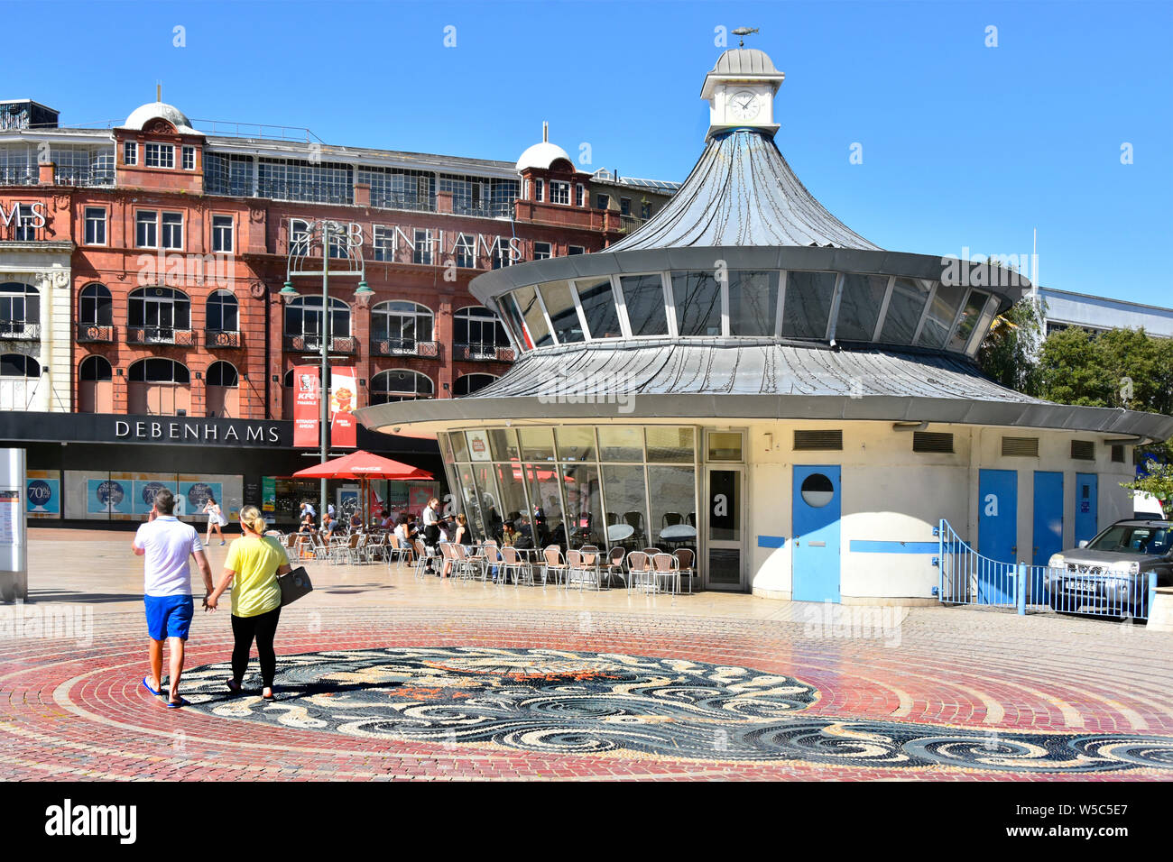 Giovane tenendo le mani a piedi in Piazza Ghiaia e pavimento in mosaico nel centro di Bournemouth con Debenhams & Obscura street cafe Dorset England Regno Unito Foto Stock
