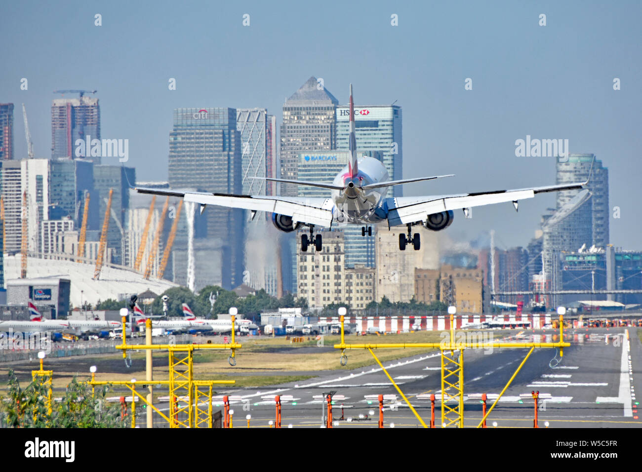 Volo British Airways in atterraggio a London City Airport (Newham) con l'O2 Arena e Canary Wharf (Tower Hamlets) skyline al di là Foto Stock