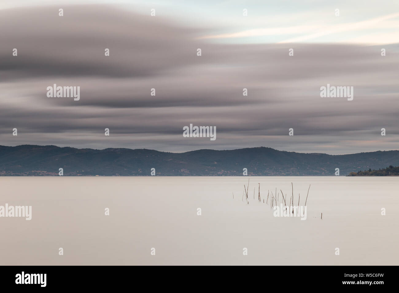 Bella lunga esposizione vista del lago Trasimeno (Umbria, Italia), ancora con acqua e nuvole in movimento Foto Stock