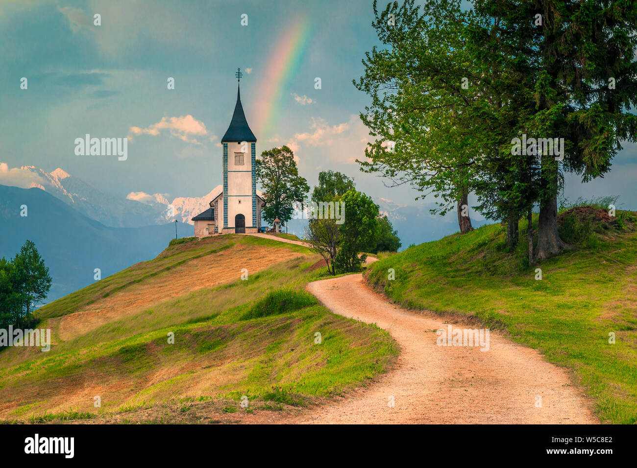 Paesaggio alpino con chiesa sulla collina. Incredibile arcobaleno colorato paesaggio e famosa Saint Primoz chiesa con alte montagne sullo sfondo, Jamnik Foto Stock