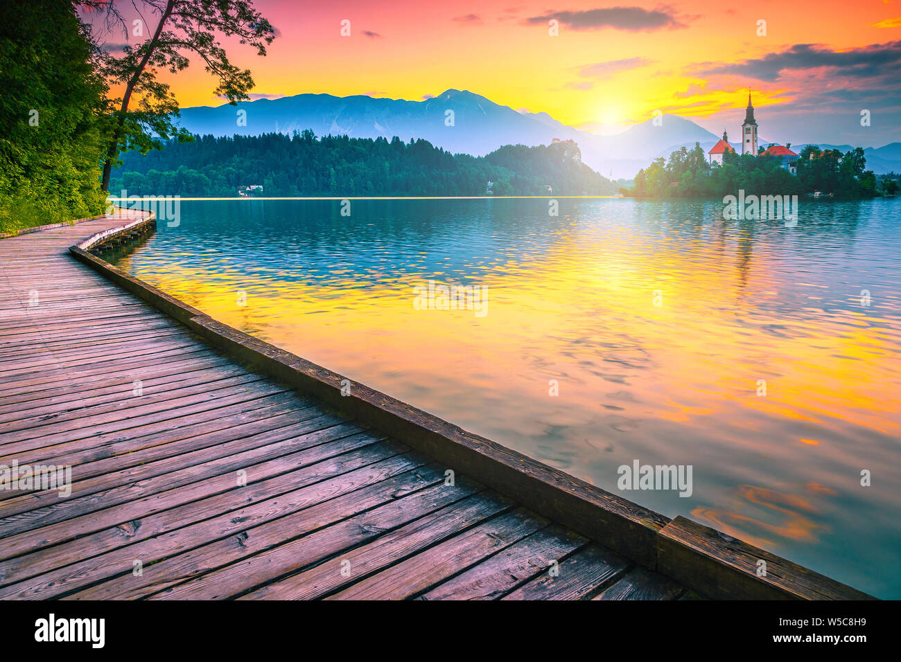 Maestosa vista la mattina con la piccola isola, la chiesa e il castello dalla passeggiata a mare di legno. Famosi viaggi e località turistica sul lago di Bled con Karavanke m Foto Stock