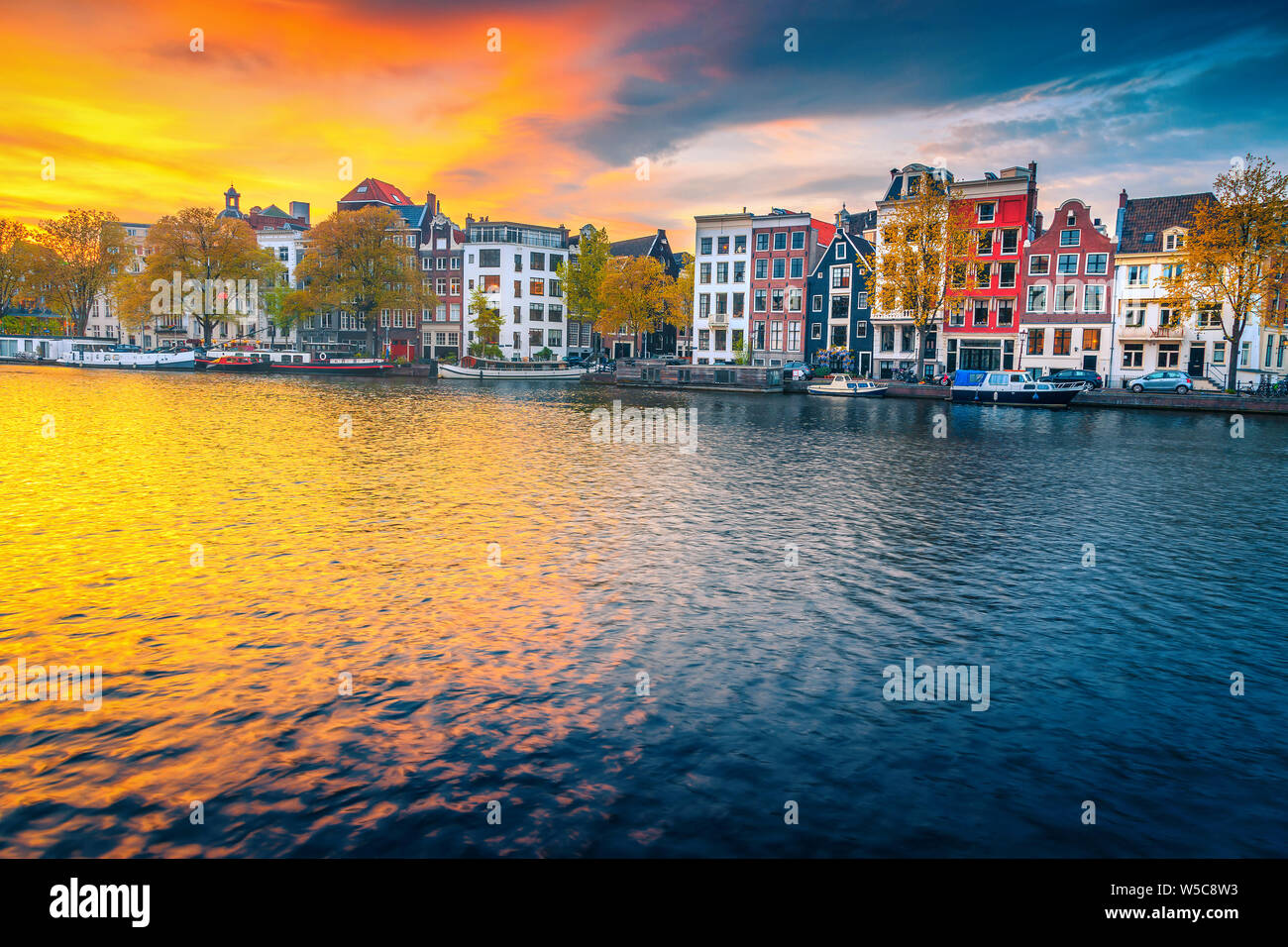 Viaggi popolari e meta turistica. Il pittoresco paesaggio urbano in autunno con case olandesi tradizionali. Canale d'acqua con case galleggianti al tramonto, Amsterdam Foto Stock