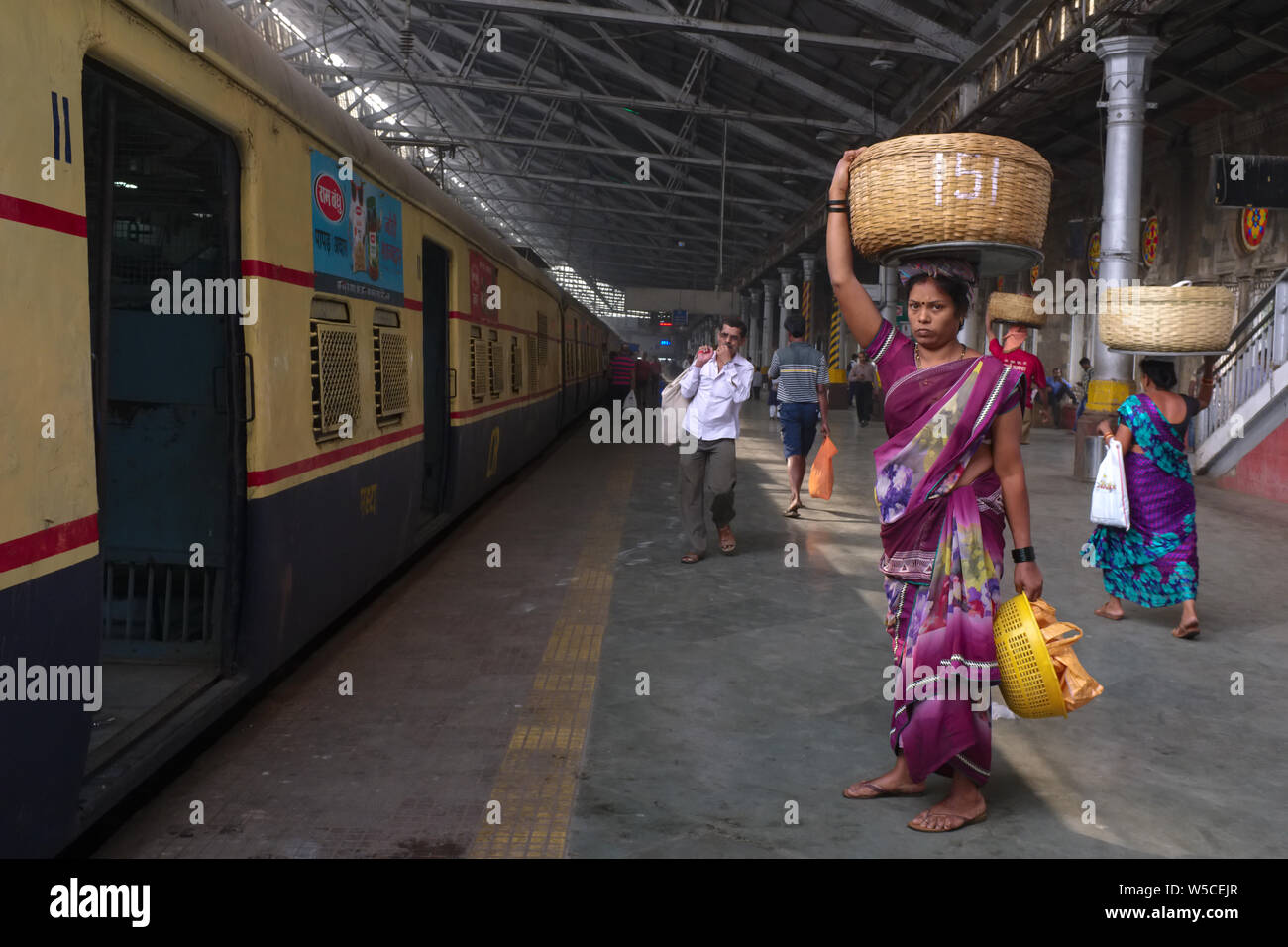 Una femmina di portiere Chhatrapati Shivaji Maharaj Terminus in Mumbai, India, portante un cestello con pesce sulla sua testa per consegnare a un treno in arrivo Foto Stock