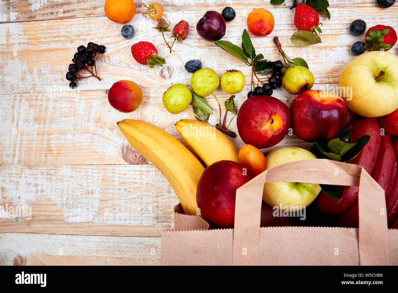 Sacchetto di carta della salute diversi frutti del cibo su sfondo di legno. Vista dall'alto. Appartamento laici tela beige sacchetto shopper caduta mentre la caduta di frutti. Foto Stock