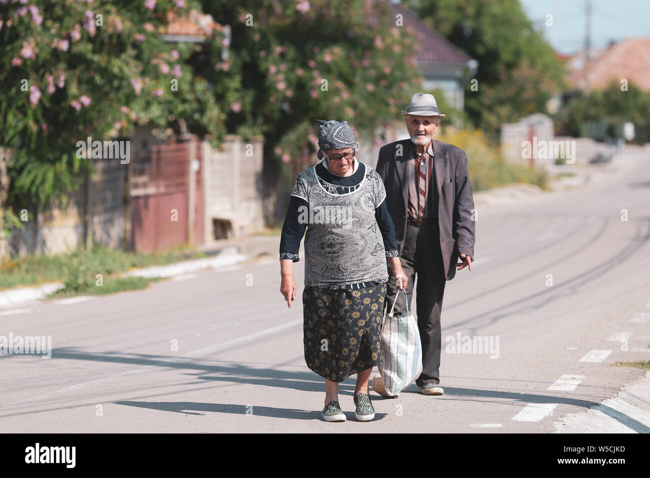 Bontida, Romania - 21 Luglio 2019: una coppia di anziani su una strada vuota in un villaggio rurale in Romania su un luminoso caldo giorno d'estate Foto Stock